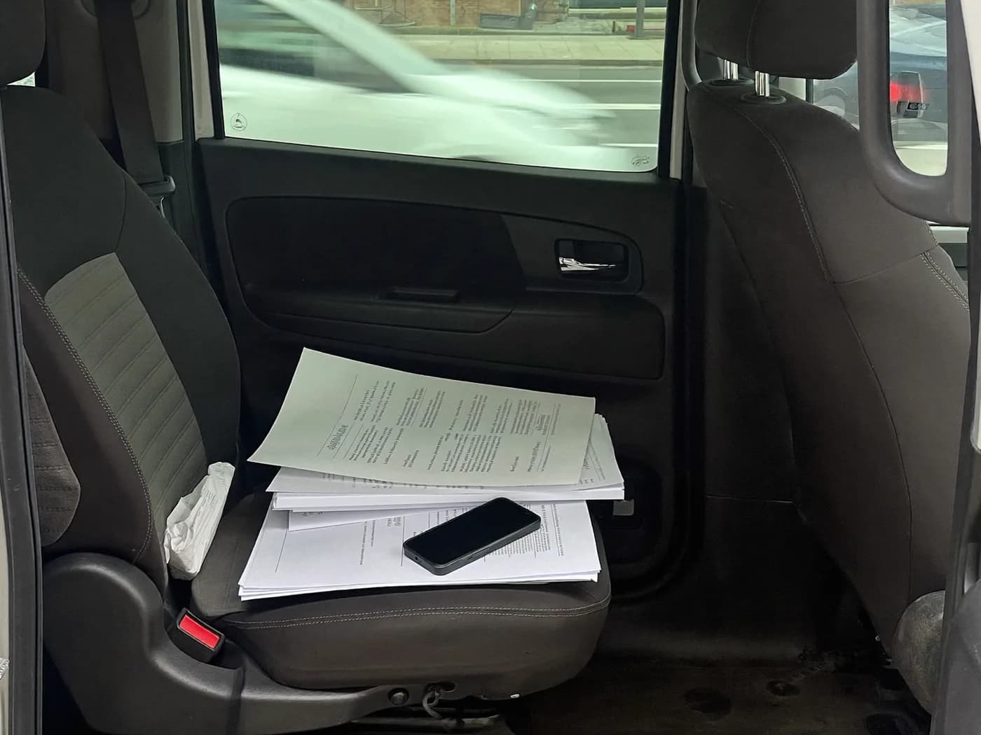 Beifahrersitz eines Transporters mit Frachtpapieren und Smartphone, Straße unscharf durch die Windschutzscheibe