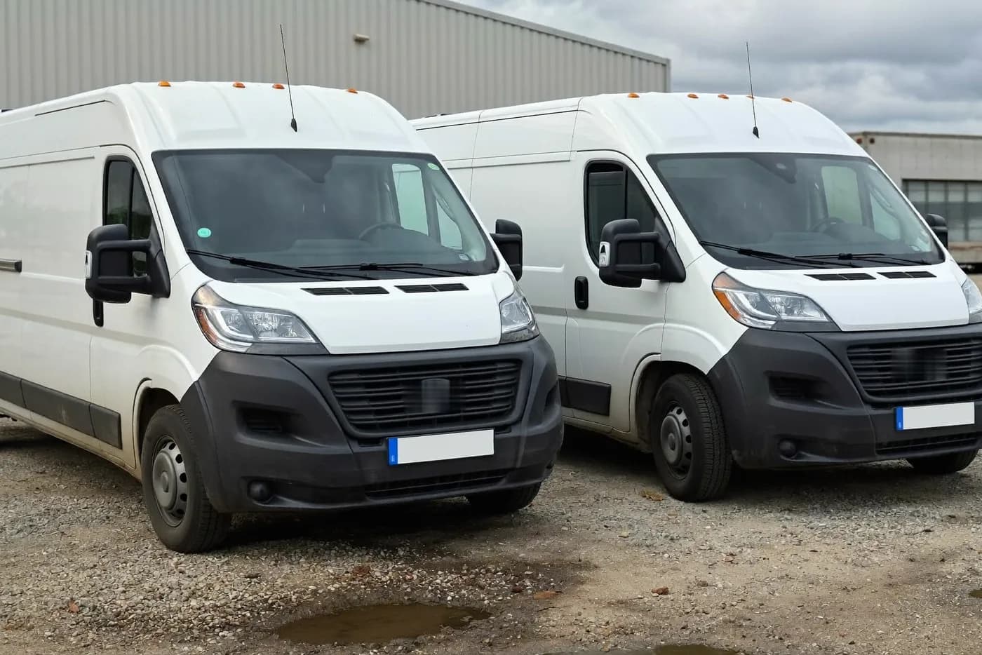 Zwei baugleiche weiße Transporter nebeneinander auf einem Betriebshof